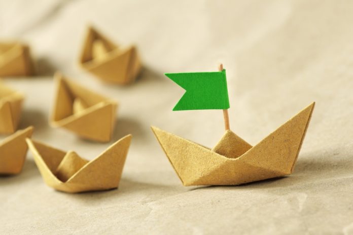 Origami,Recycled,Paper,Boat,With,Green,Flag,Leading,A,Group