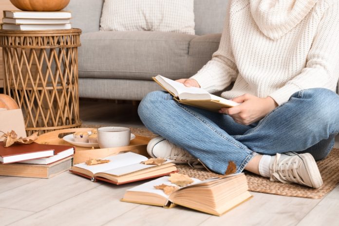 Woman,Reading,Book,With,Autumn,Leaves,On,Rug,At,Home