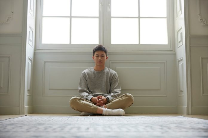 Young,Asian,Man,Sitting,On,Floor,At,Home,Legs,Crossed