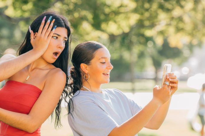 Girl,With,Phone,Spying,On,Her,Friend's,Mobile,Phone,Or