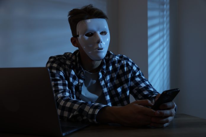 Anonymity.,Masked,Man,With,Smartphone,And,Laptop,At,Table,In