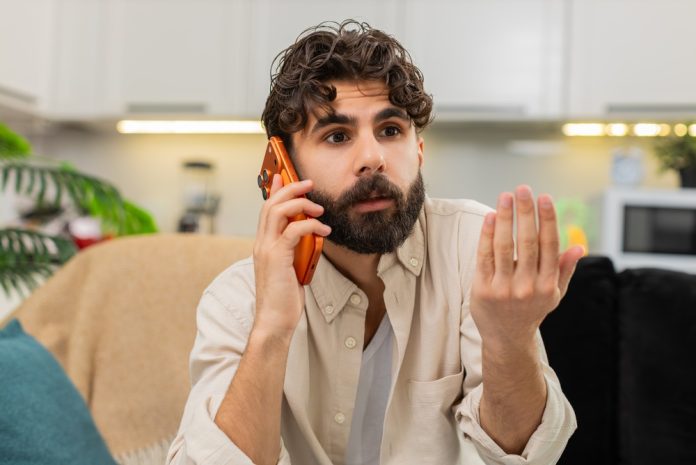 Indian,Man,At,Home,Looks,At,Smartphone,Gets,Spam,Call
