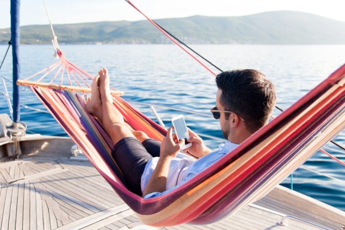Man,With,Mobile,Phone,Relaxing,On,Yacht,In,Hammock.,Sea
