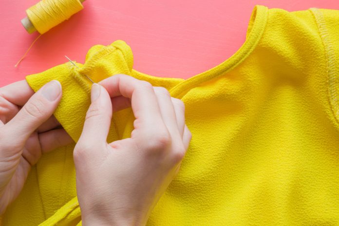 Hand,With,A,Needle,And,Thread,Sewing,A,Yellow,Blouse