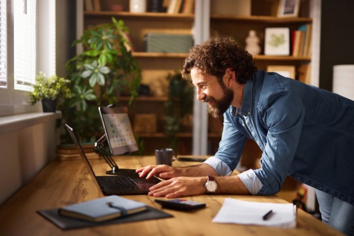 A,Man,Is,Smiling,While,Working,On,His,Laptop,In